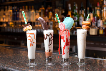 Yummy four glass of strawberry, chocolate, vanilla & caramel milkshakes or smoothies on a counter shelf..