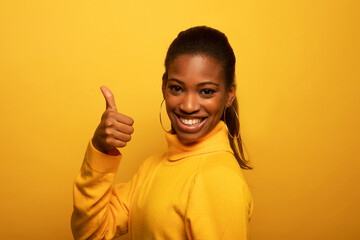 Beautiful young african woman signaling ok, isolated over yellow background