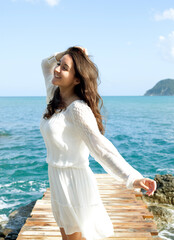 Fototapeta na wymiar Young happy woman wearing white dress posing near sea