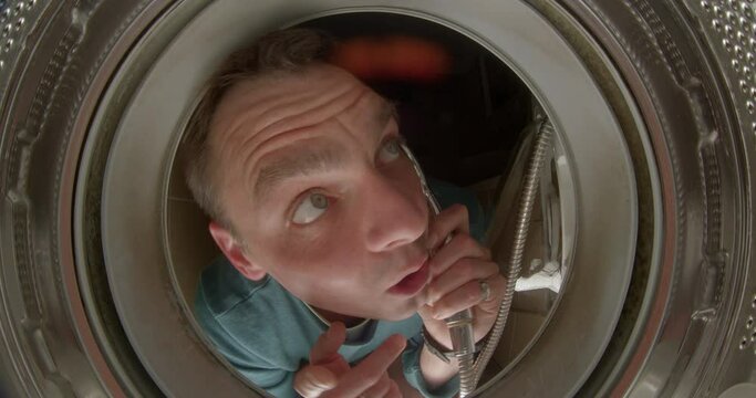 Call for a washing machine repair. A man Makes a call, points to a broken drum, looks inside. Phone handset on the wire.