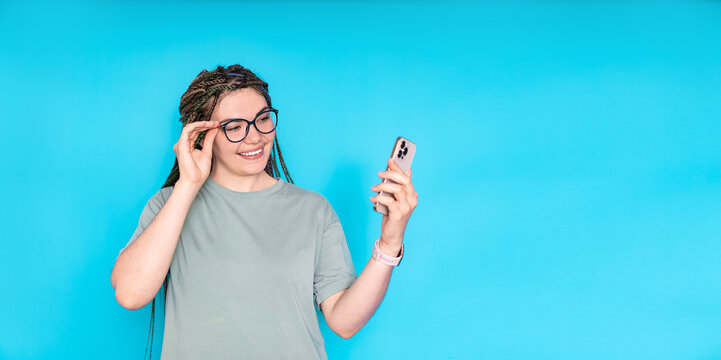 A young girl with dreadlocks on her head takes a selfie with a mobile phone on a blue background
