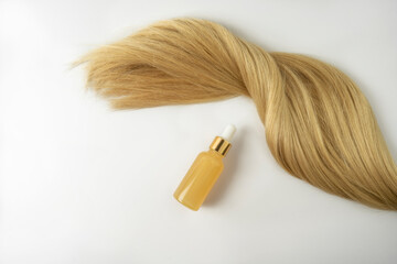 A natural oil or serum for hair care and a ply of blonde hair lying on a white background