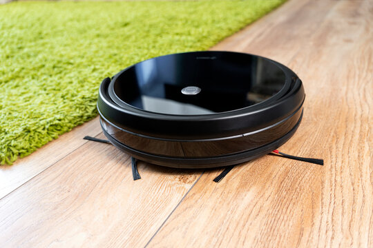 Automatic Robot Vacuum Cleaner In Black On Green Shag Carpet. New Modern Technologies For Apartment Cleaning. Smart Home Electronic Assistant