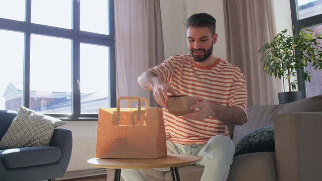 consumption, eating and people concept - smiling man unpacking takeaway food in paper bag at home