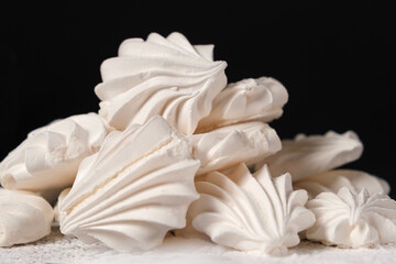 Airy sweet meringue on powdered sugar on a black background close-up, side view.