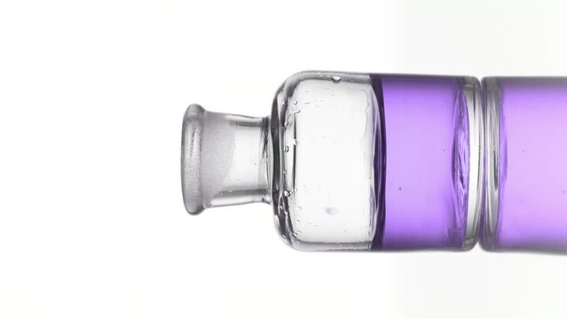 Drop of lavender oil is falling down into transparent old fashioned bottle with violet clear liquid on white background | Abstract body care cosmetics with lavender oil formulating concept