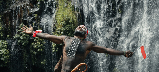 Expressive Papua man wearing traditional clothes of Dani tribe, red-white headband and bangle is...