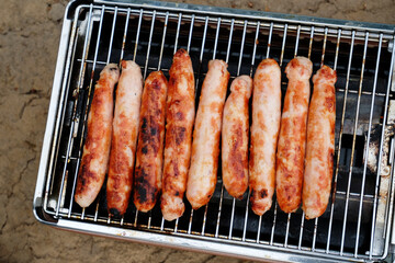 Sausages baked on a gas grill grate close-up top view. BBQ, picnic, barbecue food