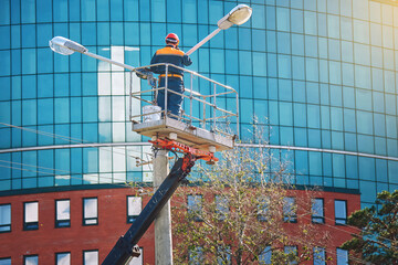 Worker work in aerial platform, man paint street light pole at height, renovation works. Man in...