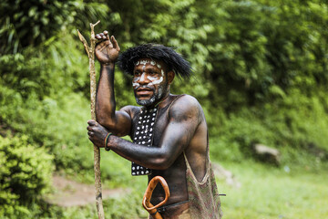 Portrait of Dani Tribe man wearing koteka, traditional clothes of Papua. Dani tribe men ready to hunt animal prey in the jungle. 