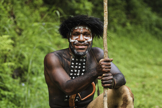Potrait of Dani tribe man from Wamena Papua Indonesia wearing traditional clothes for hunting is smiling against blurred greenery forest background.