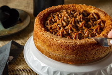 man hand cutting a slice of typical brazilian churros cake with dulce de leche, on a table, comfortable breakfast or snack scene