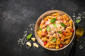 Italian pasta alla arrabiata with basil and parmesan cheese on dark table. Fusilli pasta with...