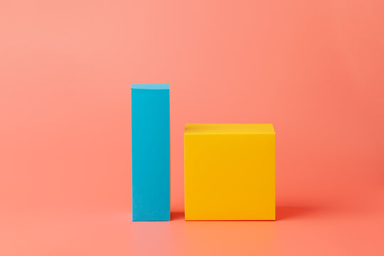 Yellow cube and blue paper rectangle. Geometric shapes made of paper or cardboard isolated on a pink background.