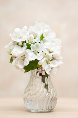 A vase of white flowers on a table against a neutral background. vertical photo