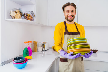 Photo of young cheerful man hold many clean plate stack good mood finish service cleaning worker house kitchen indoors