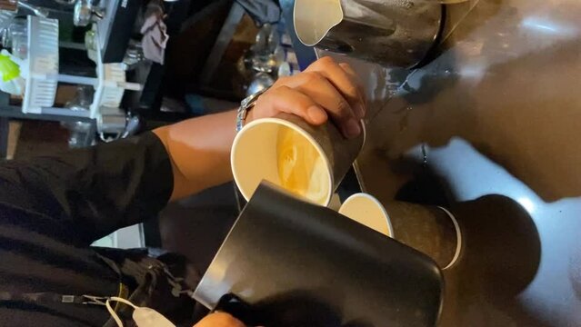 Closeup image of male hands pouring milk and preparing fresh cappuccino, coffee artist and preparation concept, fresh morning coffee