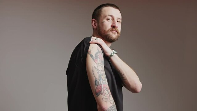 30s Caucasian man raises sleeve and shows off tattoos on arm grey background studio shot copy space . High quality 4k footage