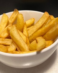 Close-up of a portion of chips in a white bowl on a black background. French fries, fast food, snack, potatoes