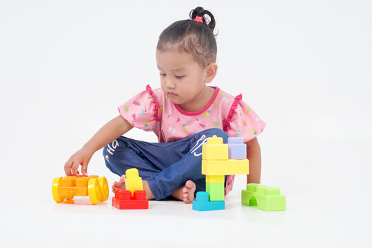 Lovely little cute asian girl playing on the floor with lots of colorful plastic blocks in studio, isolated on white background