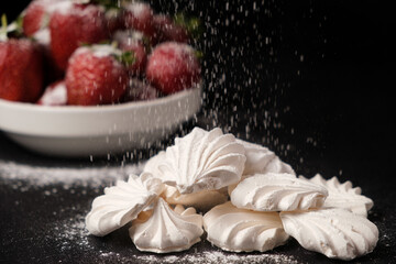 Powdered sugar falls on meringue and strawberries on a black background.