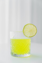 faceted glass with natural lemonade and slice of lime on grey background.