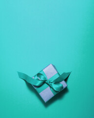 Brown paper gift box with a cyan satin ribbon bow on top on cyan background. Christmas holiday mother and father Valentines days and birthday present flat lay concept with copy space.