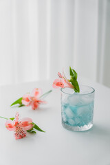 glass with cold tonic and pink alstroemeria flower on white tabletop and grey background.