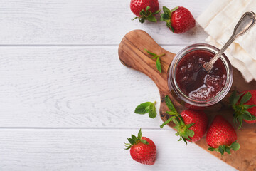 Strawberry jam. Strawberry jam in glass jar with fresh berries plate on white wooden table background, closeup. Homemade strawberry fruity jam. Top view with copy space.