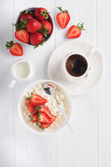 Cottage cheese with strawberries. Breakfast from cottage cheese with slices fresh strawberries, cream, cup of coffee in white bowl on white wooden background. Top view. Food concept. Mock up.