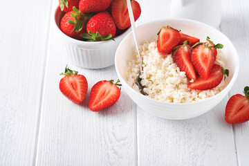 Cottage cheese with strawberries. Breakfast from cottage cheese with slices fresh strawberries, cream, cup of coffee in white bowl on white wooden background. Top view. Food concept. Mock up.