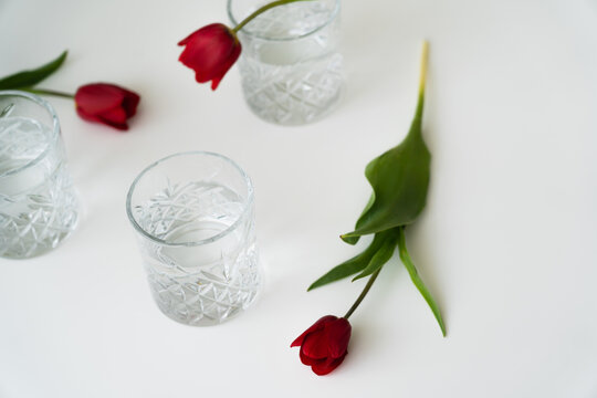 high angle view of blurred tulips and glasses with pure water on white tabletop.