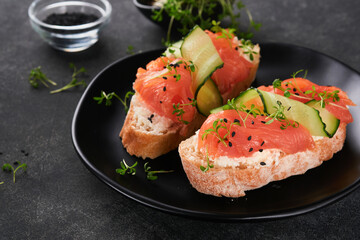 Sandwiches. Salmon toast with cream cheese, cucumber, black sesame and microgreens on black background. Seafood. Healthy food. Photography in low key. Top view.