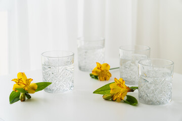 yellow alstroemeria flowers near faceted glasses with clear water on white background.