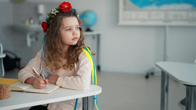 Little sad Ukrainian girl sitting in classroom during class, concept of enrolling Ukrainian kids to schools.