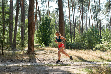 Side view of sportswoman running in green forest