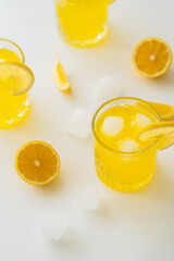 high angle view of glasses with iced citrus tonic and cut lemons on white surface.
