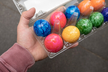 Male hand holds a transparent tray with bright colored Easter eggs, against the background of a black table. 