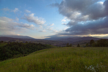 Travel photo of Ukrainian Carpathians. Scenic views of the mountain ranges during sunset, the sky with clouds and the settlements of local residents.