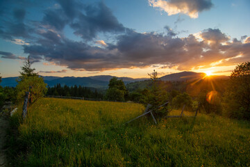 Travel photo of Ukrainian Carpathians. Scenic views of the mountain ranges during sunset, the sky with clouds and the settlements of local residents.