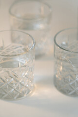 close up view of faceted glasses with clean water on blurred grey background.