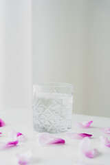 floral petals near glass with fresh water on grey background with copy space.