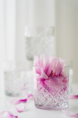 close up view of transparent glass with tonic and petals on blurred grey background.