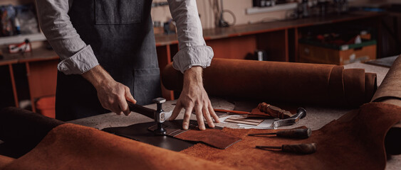 Tailor processing hammers seam on leather goods, banner Handmade craftsman