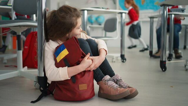 Little sad Ukrainian girl sitting on floor at school, concept of enrolling Ukrainian kids to schools.