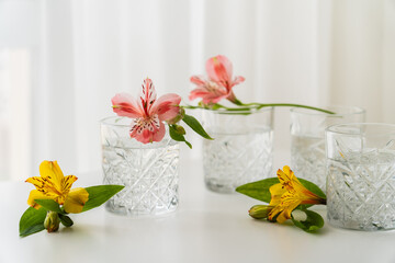 yellow and pink alstroemeria flowers near glasses with water on white tabletop.