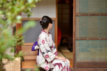 京都町屋の縁側に座りたたずむ浴衣を着た若く美しい女性の後ろ姿