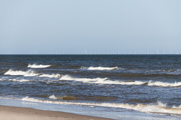 Meer mit Brandung und Offshore-Windpark im Hintergrund