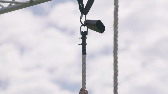 Rope climber rings cowbell at top of rope during military obstacle course training race close up slow motion 4k