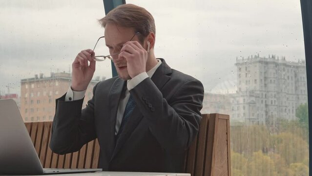 Businessman working using laptop, cowering area, city on background, rainy autumn weather.